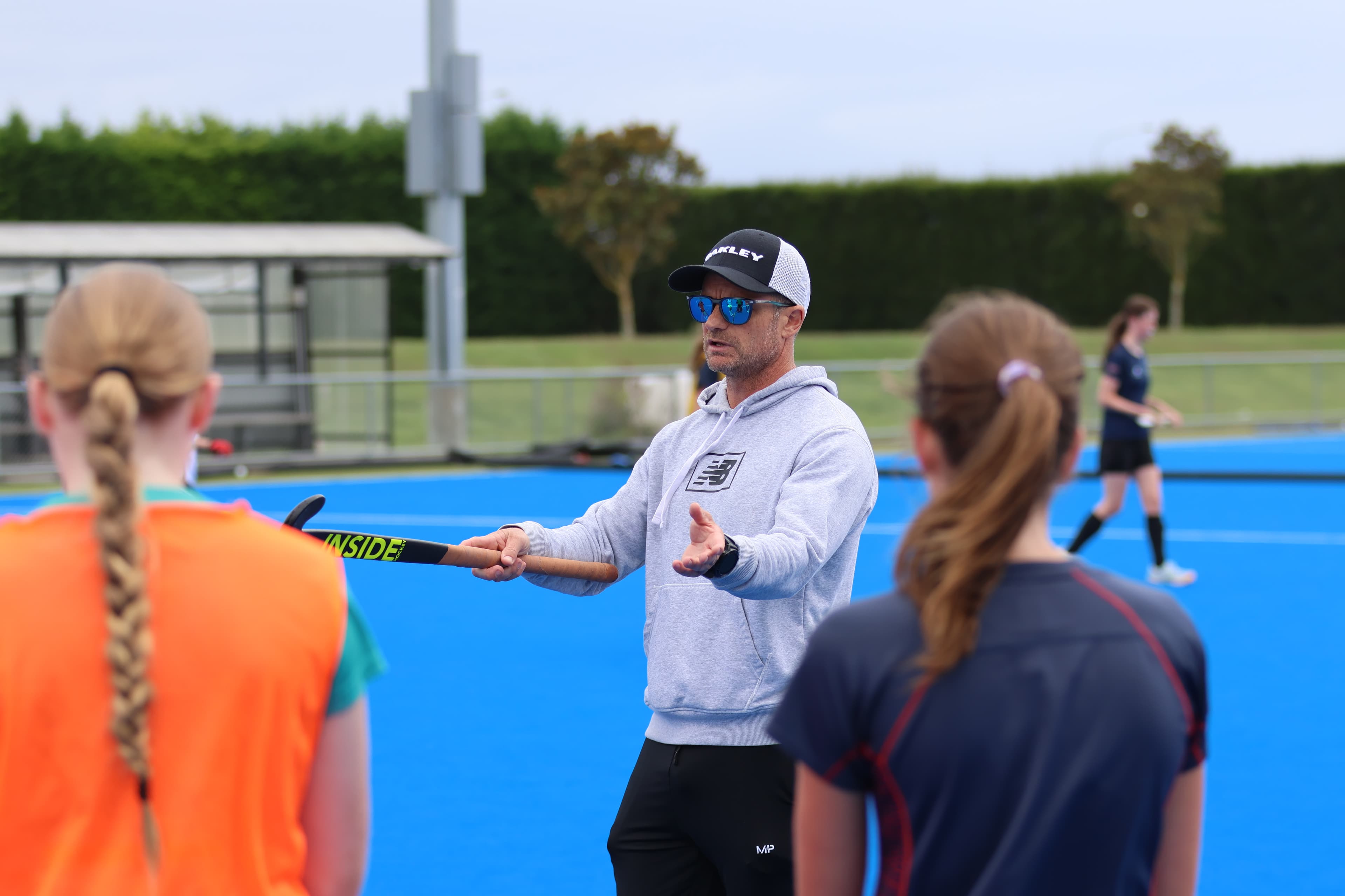 A hockey coach explaining a technical point to two players on the turf.
