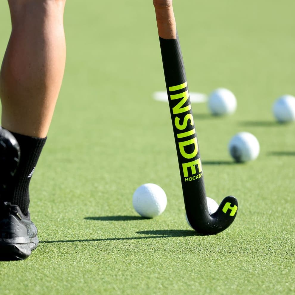 An Inside Hockey stick beside hockey balls on turf.